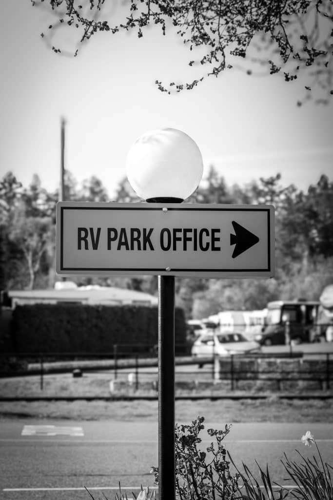 Black and white photo of RV Park Office directional sign with round lamp post.