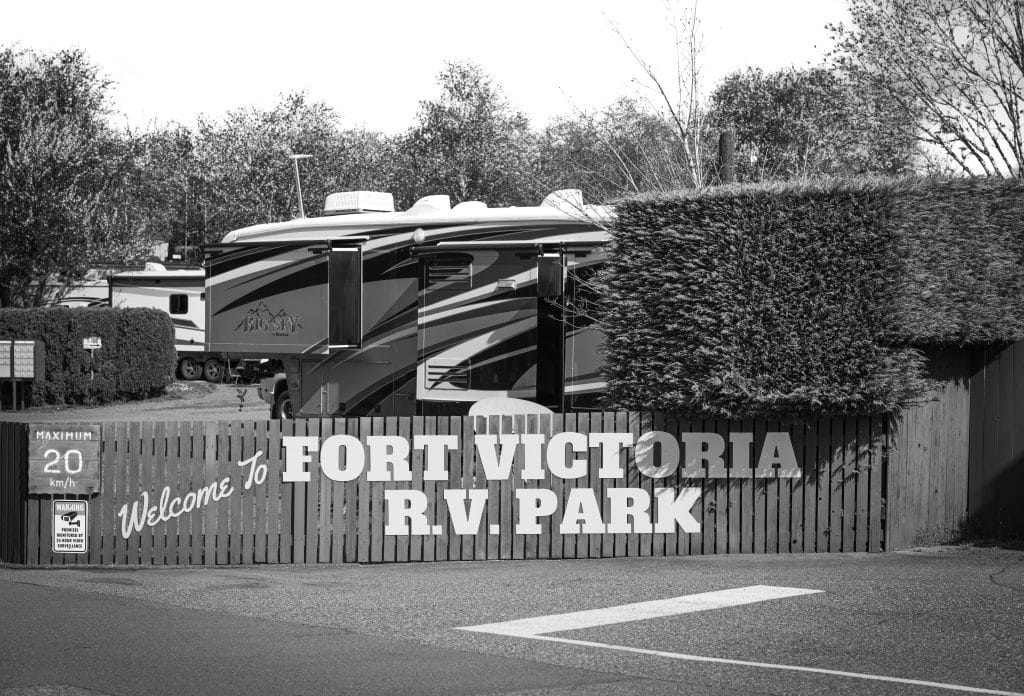 Black and white photo of the Fort Victoria RV Park entrance sign with RVs in the background.