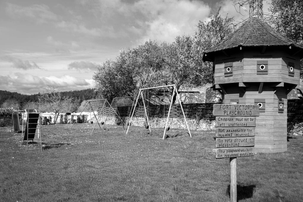 Black and white photo of the playground beside the historic blockhouse at Fort Victoria RV Park.